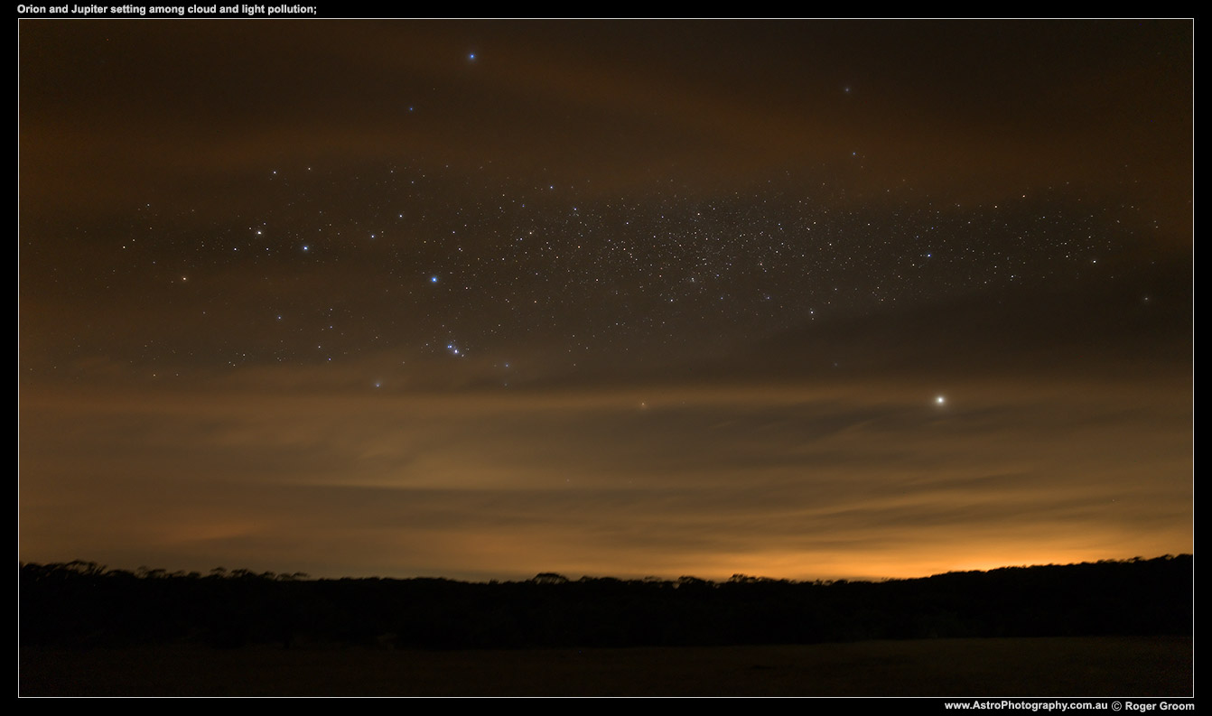 Orion and Jupiter setting among cloud and light pollution.