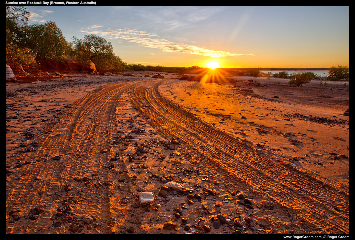 Sunrise over Roebuck Bay (Broome, Western Australia). The golden sun catches pebbles on the red sand of the beach.